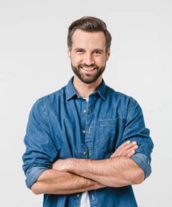 Confident caucasian young man in casual denim clothes with arms crossed looking at camera with toothy smile isolated in white background